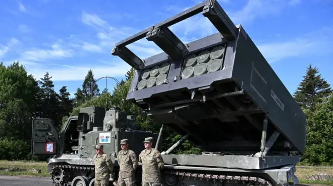 İngiliz Ordusu'na bağlı 1. Royal Horse Artillery birliğinin askerleri, 20 Temmuz 2022 tarihinde Almanya'nın güneyindeki Eschenbach yakınlarında bulunan Grafenwöhr'de düzenlenen "Dynamic Front 22" tatbikatı sırasında, zırhlı ve kendinden tahrikli bir M270 Çok Namlulu Roketatar Sistemi (MLRS) önünde duruyor.