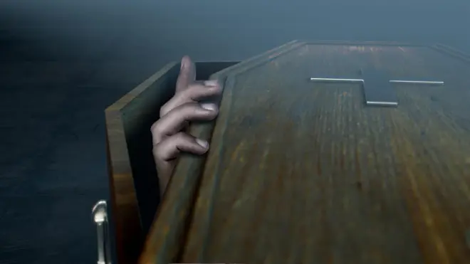 Mão de pessoa dentro de caixão tentando abrir a tampa do mesmo