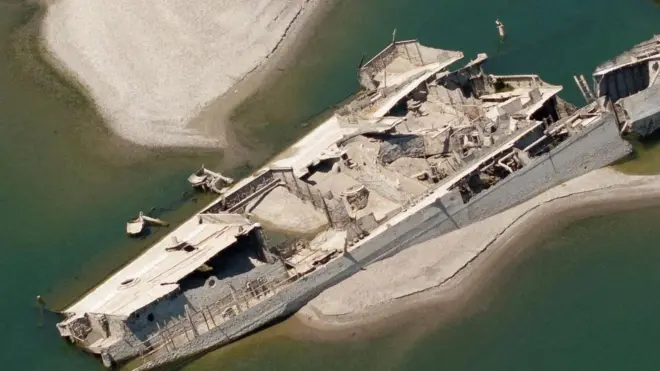 A large shipwreck is visible next to a white sandbank in green waters.