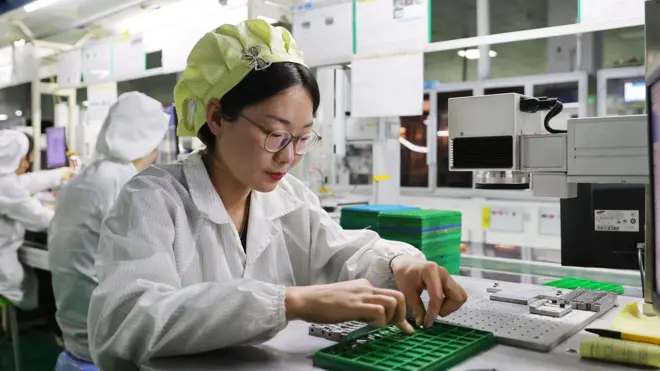 Una mujer ensambla manualmente piezas para teléfonos móviles en una fábrica