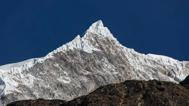 A panomanic view of the Langtang Lirung peak. The snowy summit is seen against a clear blue sky.