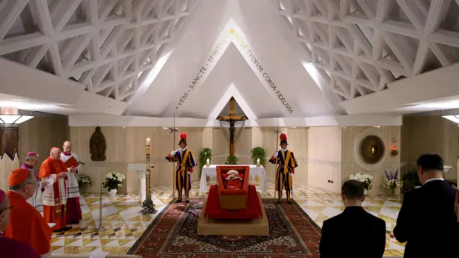 Папа Франциск в открытом гробу в окружении нескольких людей.