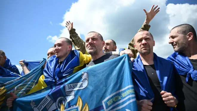 Колишні полонені з українськими прапорами на плечах, обіймаючись, фотографуються на згадку.  