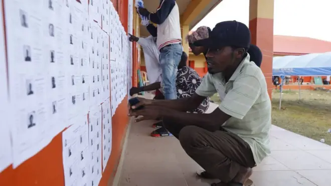 Man dey check list of eligible voters dem post for wall