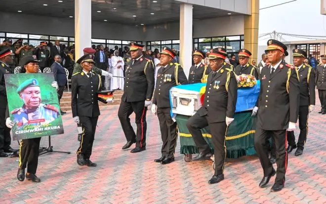 Abasirikare baherekeje isanduku y'abapfiye iriho indabo n'ibendera ry'igihugu n'undi uri imbere afite ifoto nini iriho Jenerali Peter Cirimwami mu muhango wo kumusezeraho