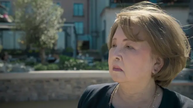 krupni kada starije žene, Japanke, koja gleda zamišljeno u stranu, iza nje mutna pozadina, ulica, drvo, kuće.