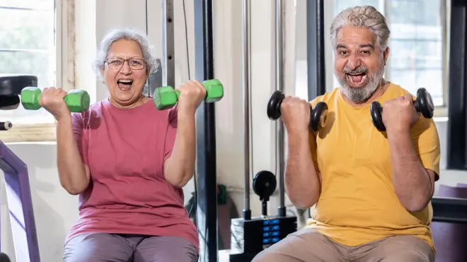 Happy indian senior couple have fun exercises in gym, Excited elderly people do weight lifting training with dumbbells at health club to stay fit. Retirement life. - stock photo