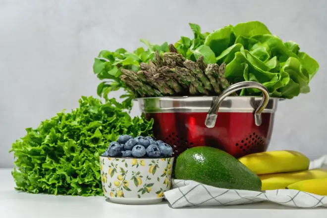 Masada süzgeç içinde taze marul, kuşkonmaz ve roka salatası, mutfak havlusu. Yaban mersini kasesi, muz ve avokado.