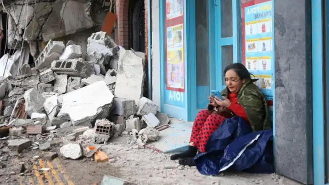 Hatay'da çöken bir binanın yanında bekleyen bir kişi
