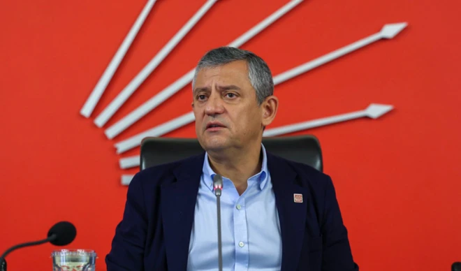 Özgür Özel parti genel merkezinde, arkada CHP okları var. Kravatsız kürsüde oturuyor.