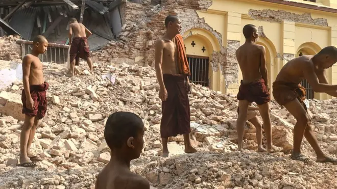 Buddhist monks stand on rubble as they clear up debris at the damaged Thahtay Kyaung Monastery in Mandalay on April 1, 2025