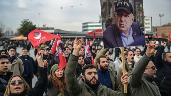 Kalabalık slogan atıyor, sakallı bir adamın elinde Ümit Özdağ'ın fotoğrafı var. 