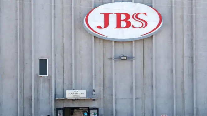 A fachada de um edifício da JBS, com o logotipo da empresa em destaque e uma placa indicando os escritórios da administração principal.