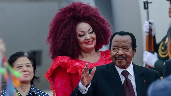 Le président camerounais Paul Biya, vêtu d'un costume noir, d'une chemise blanche et d'une cravate bordeaux, salue à son arrivée à l'aéroport international de Pékin, où il se rend pour assister au sommet du Forum sur la coopération sino-africaine (FOCAC) à Pékin, en Chine, le 4 septembre 2024. Son épouse, Chantal, vêtue d'une robe rouge, se tient à ses côtés