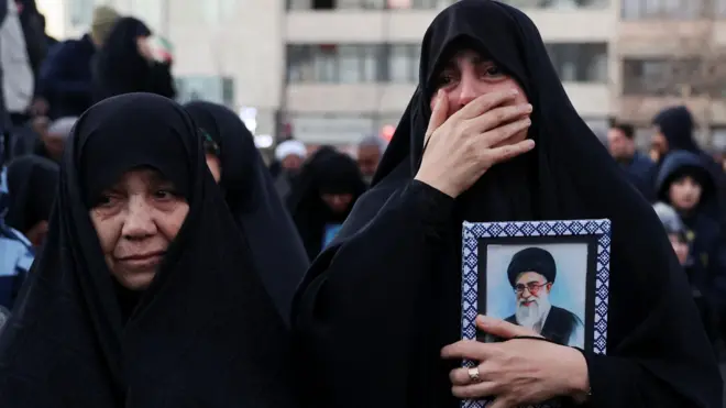 Two women in black at a rally in Tehran. One holding a portrait of the assassinated Ayatollah Ali Khamenei and crying