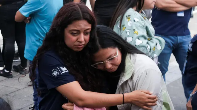 Dos mujeres se abrazan luego de evacuar su lugar de trabajo por un terremoto.