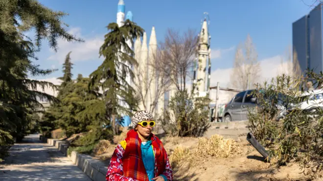 طهران، إيران – 16 يناير/كانون الثاني 2026: تمرّ امرأة بجانب صواريخ معروضة في معرض دائم للأسلحة في طهران. 