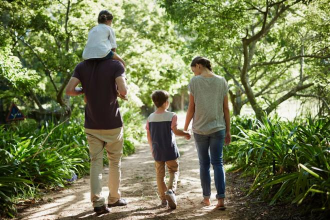 Família com dois adultos e duas crianças caminhando de costas par a câmera em jardim
