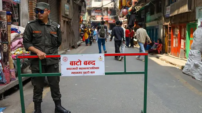 काठमाण्डू महानगर प्रहरीका एक कर्मचारी 'बाटो बन्द' लेखिएको बोर्डसँगै