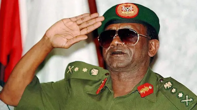 Aworan Ọgagun Sanni Abacha, olori ilẹ Naijiria nigba kan ri, o wọ aṣọ ologun pẹlu diigi loju, o si gbe ọwọ sori rẹ lati jẹjẹ