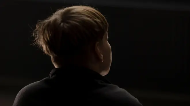 Мальчик-подросток в темной кофте спиной к камере и на темном фоне