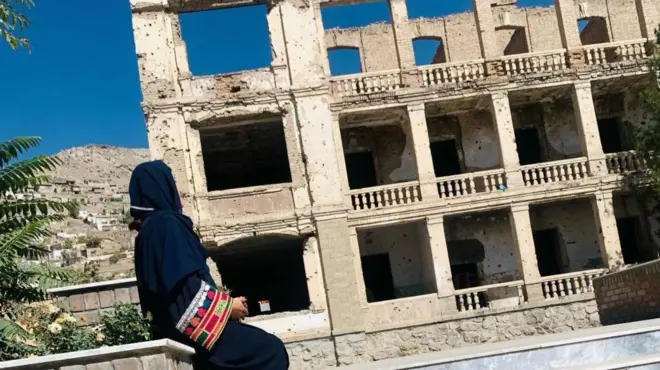 منظر جانبي لنادية بالحجاب الأسود أمام مبنى متضرر