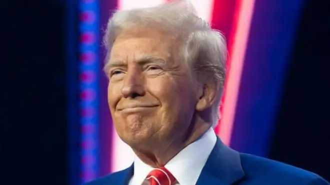 US President-elect Donald Trump smiling in front of red, white and blue lights.