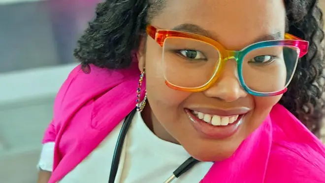 Celiwe Ndaba nu gakoti ka rose, amarori asa n'umunywamazi na
stethoscope mw'izosi, ariko aramwenyura yifata agafoto