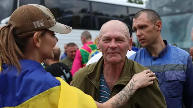 Укрнаинский военный и девушка с украинским флагом на плечах, на заднем плане еще один военный 
