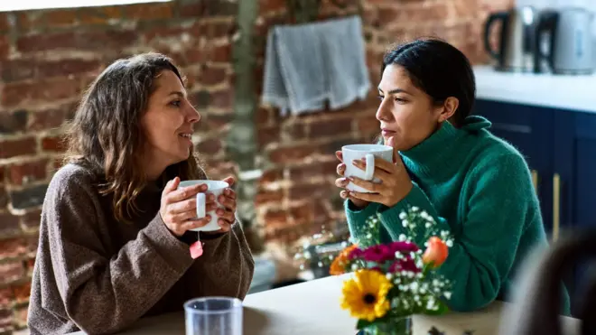 Dos mujeres conversan con una taza de te en la mano.