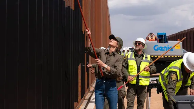 A secretária de Segurança Interna dos EUA, Kristi Noem, segura um pau usado para pintar de preto muro fronteiriço 