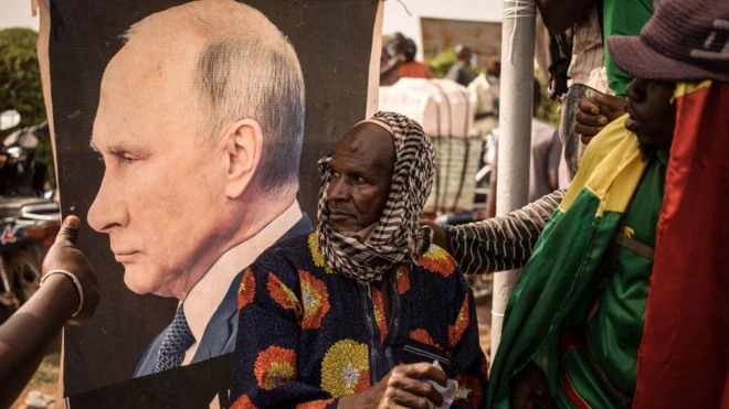 Мужчина в куфии на фоне баннера с портретом Путина