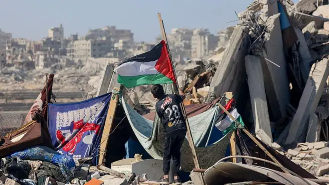 پسربچه‌ای در حال نصب پرچم فلسطین را در میان ویرانه‌ها در خان یونس در جنوب غزه 