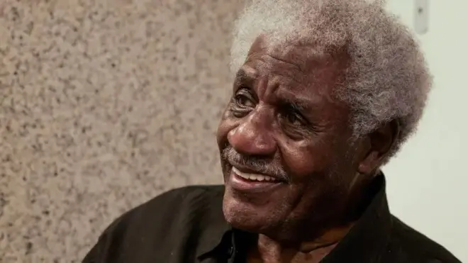 Tony Tornado é um homem negro de cabelos brancos. Na foto ele está sorrindo e olhando para o lado