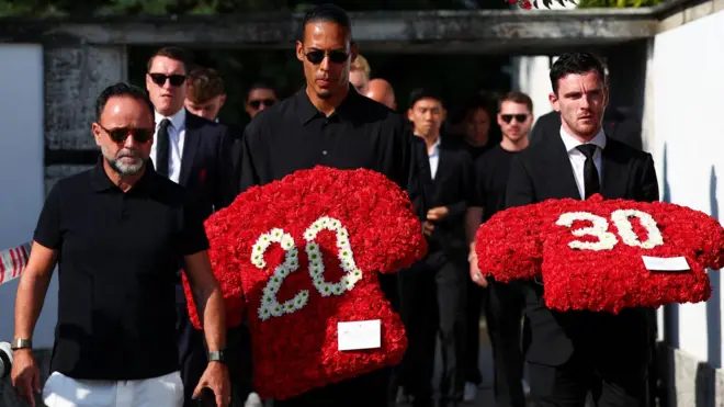 Grupo com roupas pretas e óculos escuros, em funeral, com coroas de flores



