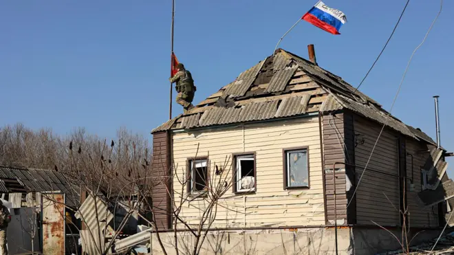 Российский солдат водружает флаг над домом
