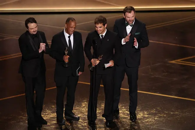 Quatros homens no palco segurando estatuetas do Oscar