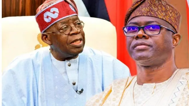 Gomina Seyi Makinde ree to jokoo lori aga gomina ipinle Oyo, o n woye pẹlu bo ṣe kawọ le tabili to wa niwaju rẹ pẹlu ẹrọ gbohùngbohùn pẹlu àwòrán Tinubu 