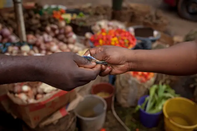 Un vendeur ambulant échange de l'argent avec un client sur un marché de légumes.