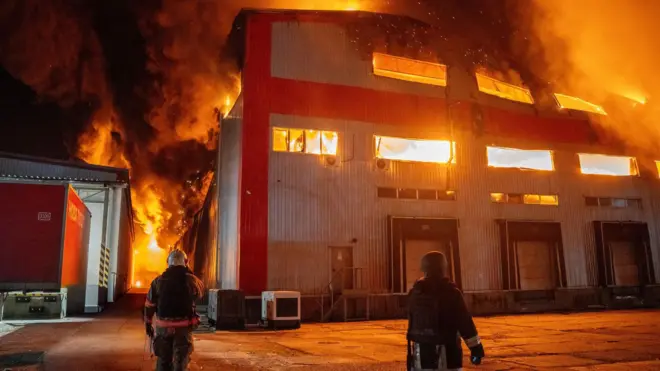 Двоє пожежних стоять біля палаючого будинку