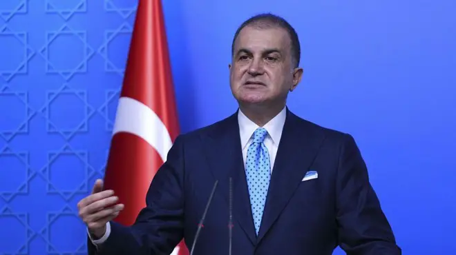 Ömer Çelik kürsüde konuşuyor. Arkasında Türk bayrağı var.