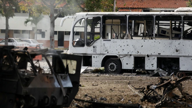 Un autobus blanco y otro vehículo, uno militar, seriamente dañados