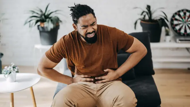 Homem com mãos na barriga e rosto demonstrando desconforto; ele está sendadotunísia futeboluma salatunísia futebolestar