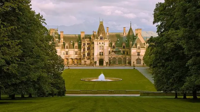 Vista panorâmica de Biltmore House, atrás de um grande jardim com árvores e uma fonte no centro