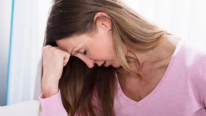 سيدة في مرحلة منتصف العمر مغمضة العينين تبدو عليها ملامح الحزن والإرهاق