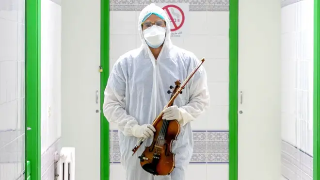 A healthcare worker in protective gear carrying a violin