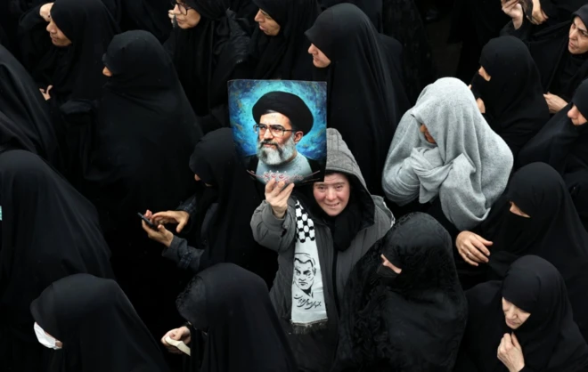 İranlı bir kadın, 18 Mart'ta öldürülen İran İstihbarat Bakanı İsmail Hattab ve ailesinin cenaze törenine katılırken, merhum İran dini lideri Ayetullah Ali Hamaney'nin fotoğrafını tutuyor.