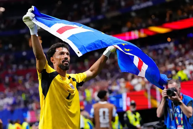 Vozinha com uma bandeira de Cabo Verde após jogo. Ele usa um uniforme amarelo.