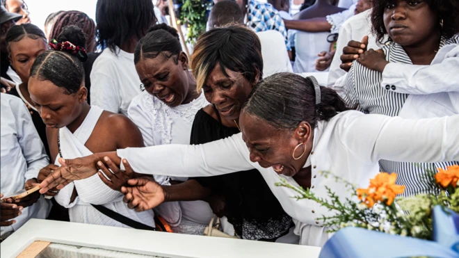 Mujeres lloran sobre un féretro que permite ver al difunto durante el funeral colectivo de ocho personas asesinadas en un ataque con drones en Puerto Príncipe, Haití, el 4 de octubre de 2025. Los drones que tenían como objetivo al presunto líder de una pandilla en un barrio de Puerto Príncipe controlado por estos grupos criminales terminaron matando a once civiles el 20 de septiembre de ese año.