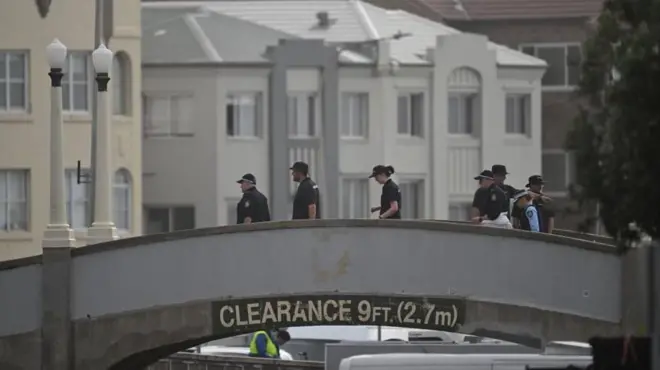 Police officers stand on a small hump-backed bridge.